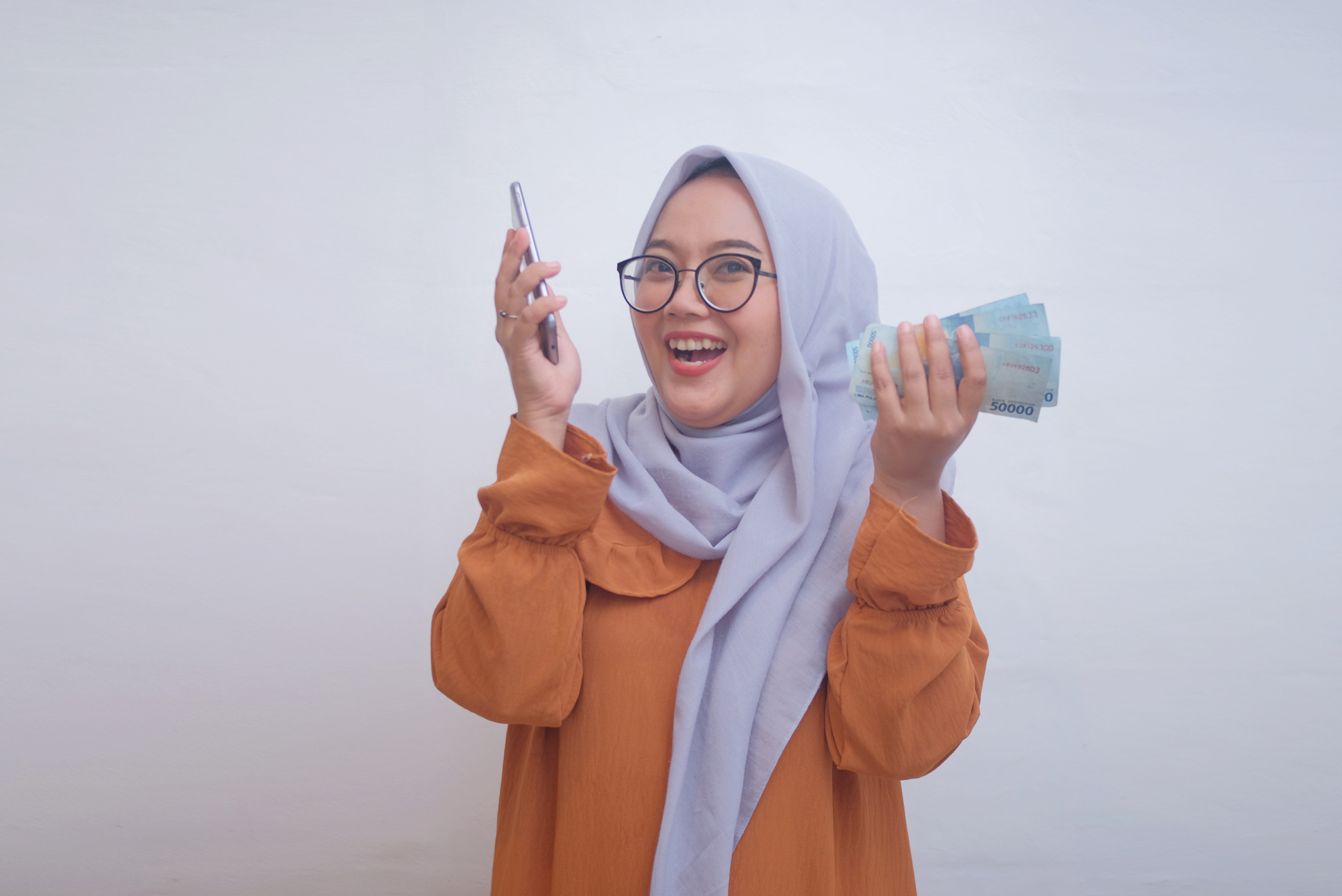 Happy Woman in Hijab Holding a Smartphone and Money